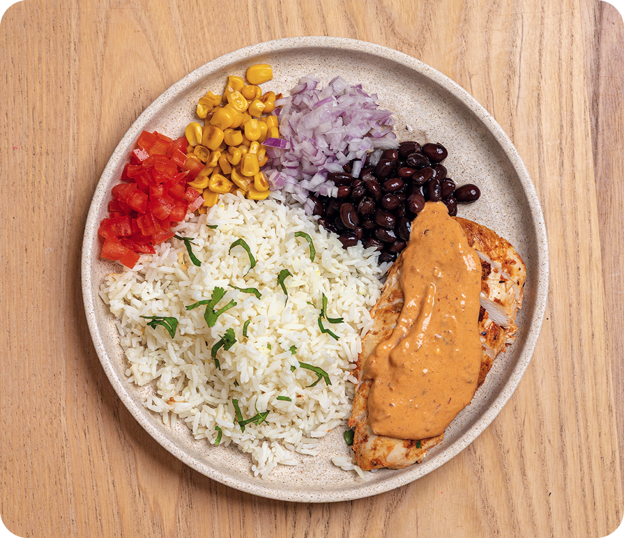 Plated meal with rice, chicken, vegetables, and sauce on a wooden surface