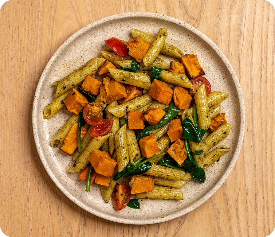 Pasta dish with vegetables on a beige plate on a wooden surface
