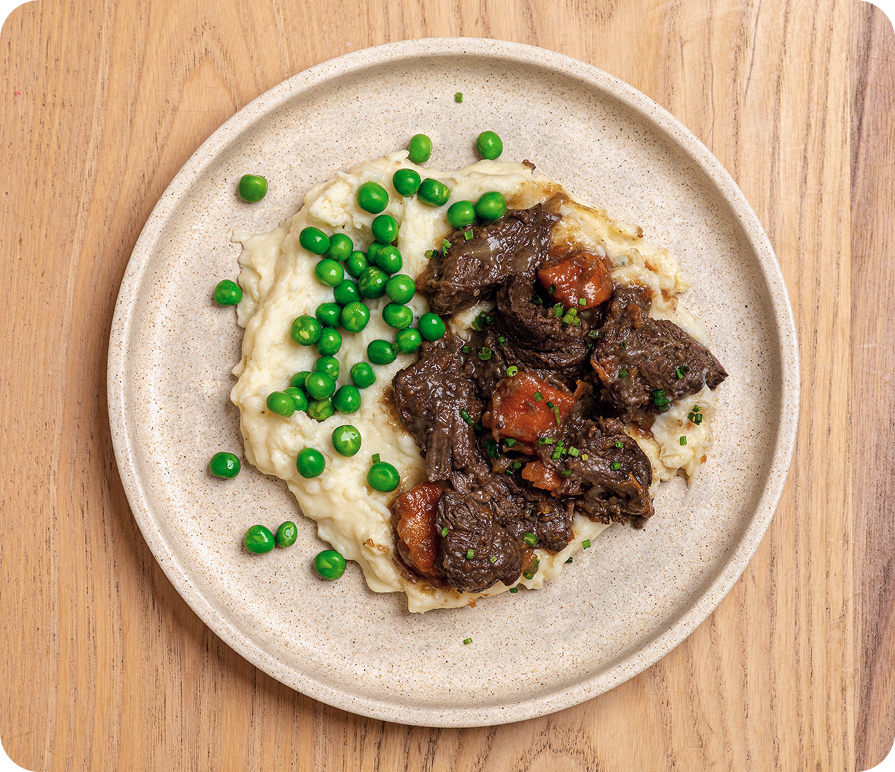 Plated dish of beef and mashed potatoes with peas on a wooden surface