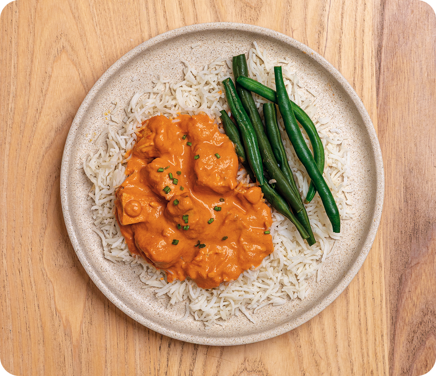 Plated dish of orange curry over rice with green beans on a wooden surface