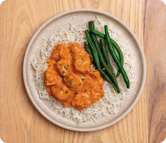 Plated dish of orange curry over rice with green beans on a wooden surface