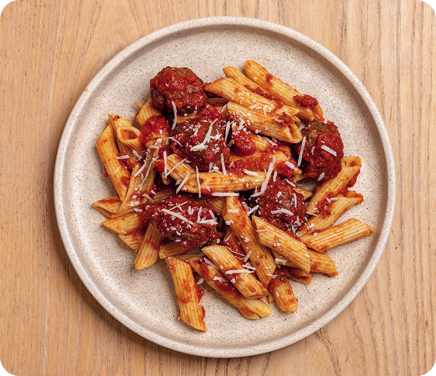 Penne pasta with meatballs on a beige plate on a wooden surface