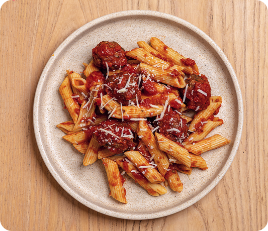 Penne pasta with meatballs on a beige plate on a wooden surface