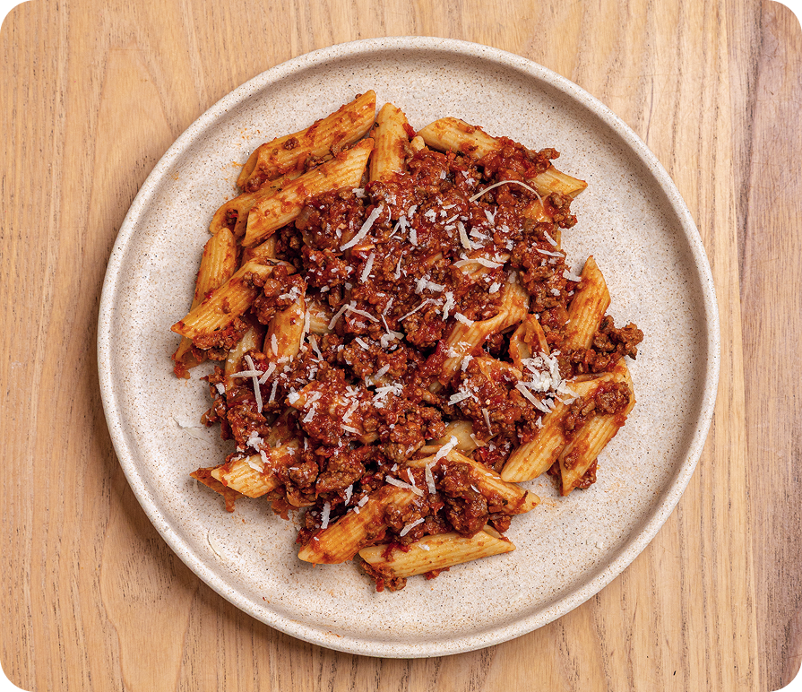 Penne pasta with bolognese sauce on a beige plate on a wooden surface