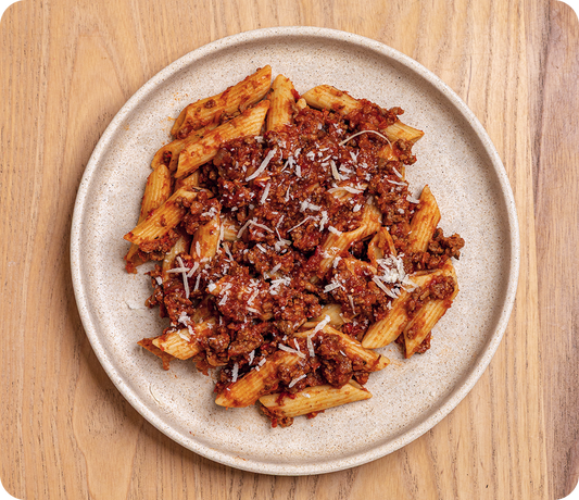 Penne pasta with bolognese sauce on a beige plate on a wooden surface