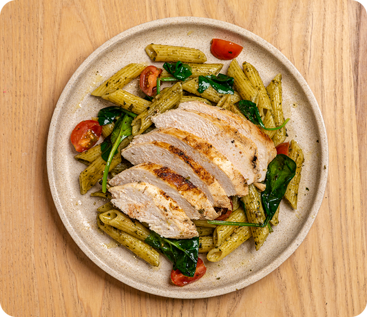 Plated dish of pasta with chicken and vegetables on a wooden surface