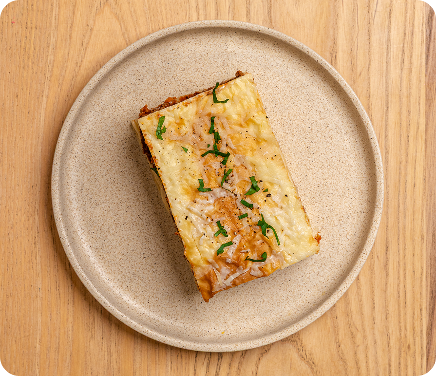 Rectangular slice of lasagna on a beige plate with a wooden background