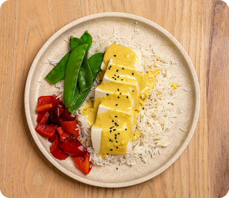 Plate of food with yellow dish, rice, and vegetables on a wooden surface